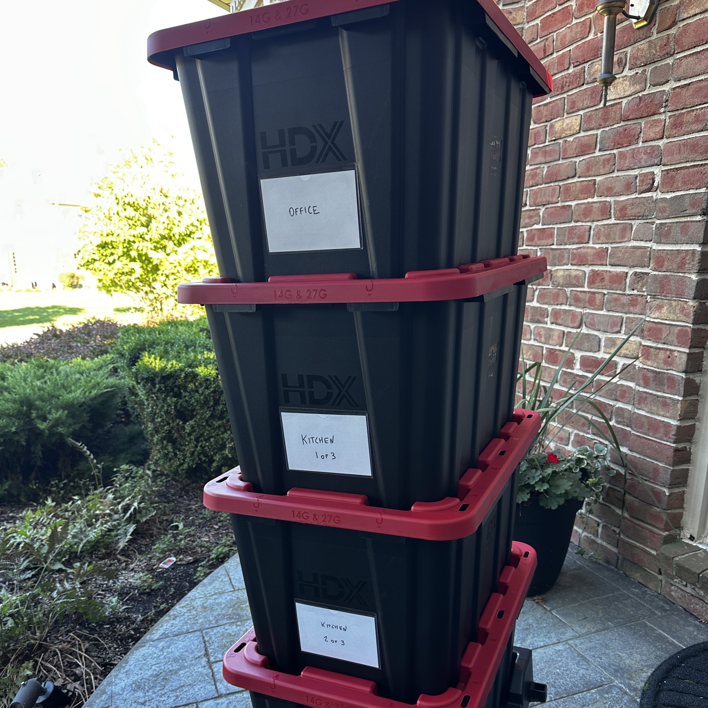 Close view of stacked black totes with red lids and handwritten room labels