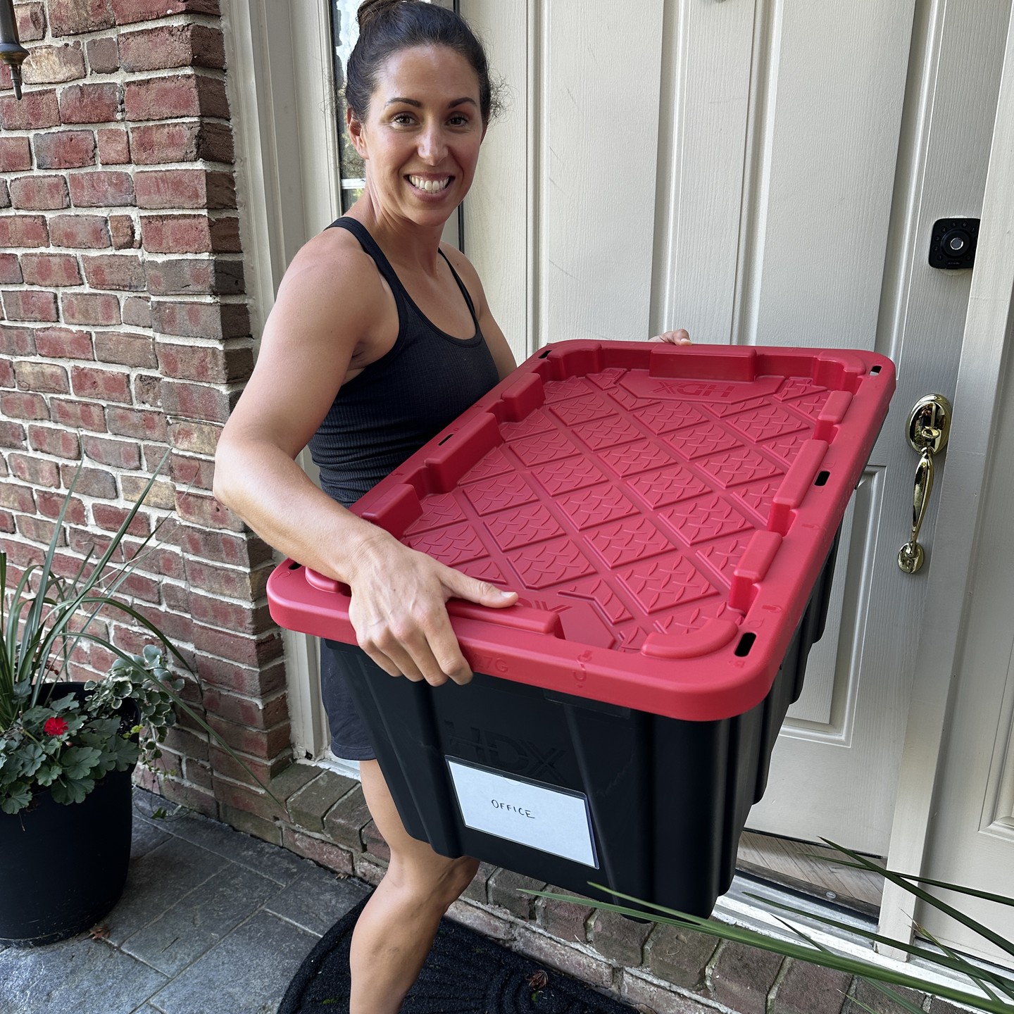 A single labeled moving tote with a red lid being carried to a front door