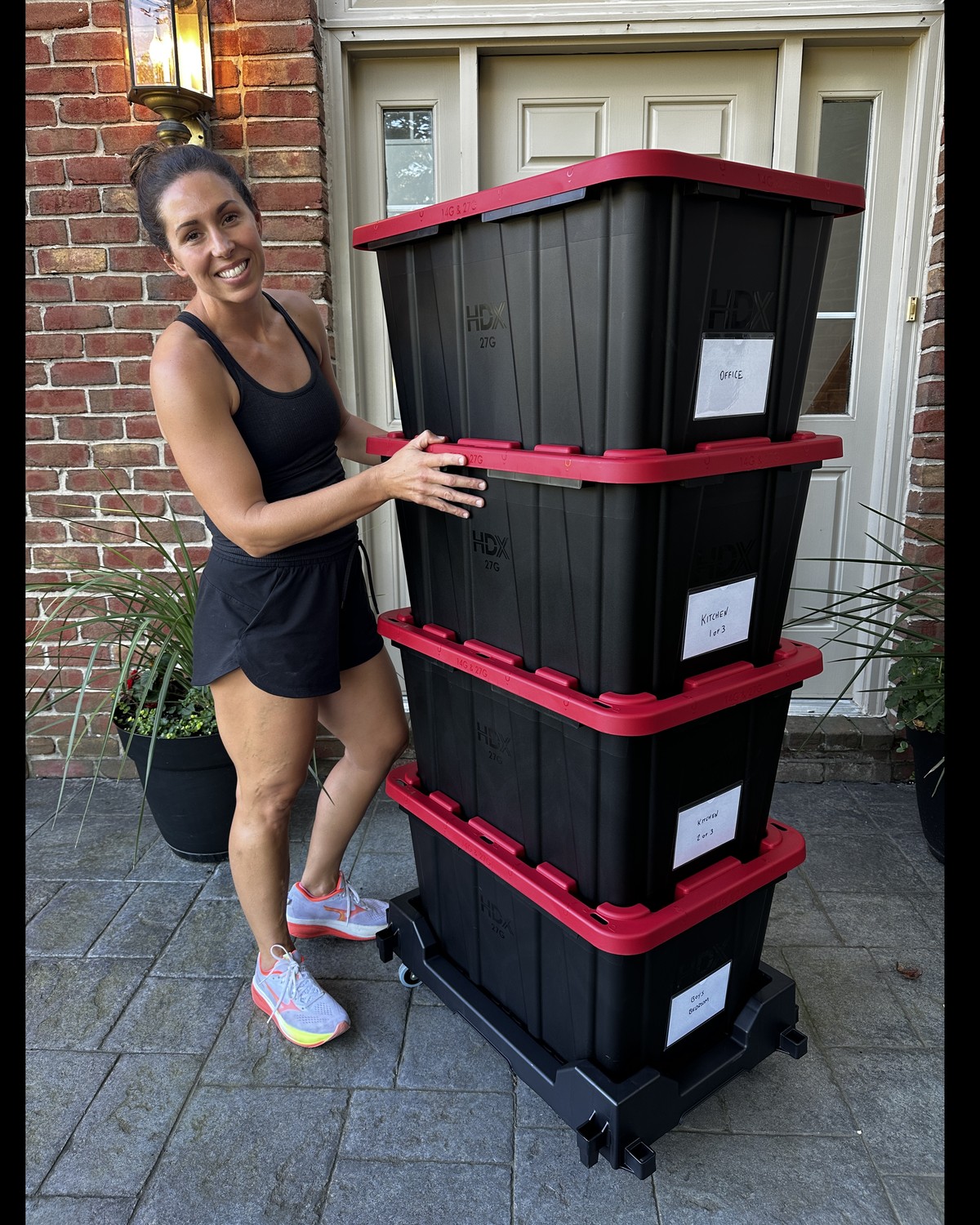 Stack of black moving totes with red lids on a rolling dolly at a front door in Northville, Michigan